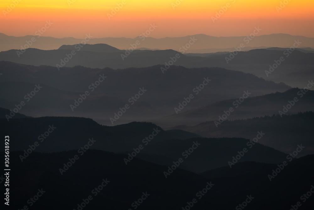 nature background with mountain silhouettes and a pine tree forest. Smooth gradient from dark to light orange caused by the long-focus lens and twilight. Carpathian mountains, Ukraine.