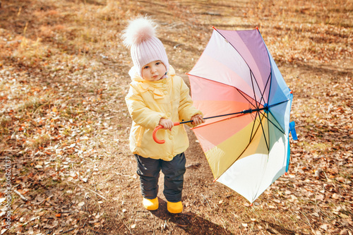 a small child in a warm suit and with a colorful umbrella walks in the woods. autumn park. The concept of children's fashion, accessories, outdoor walks