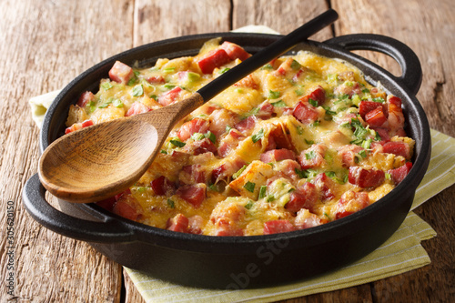 Fotografie Tasty hot homemade strata with ham, onions, cheese and eggs close-up in a pan on the table