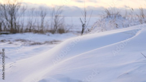 Small snow particles fly over snowbank, driven by cold wind. Severe weather at winter time, strong low flow move piercing flakes at ground level, windy shore of lake or frozen sea photo