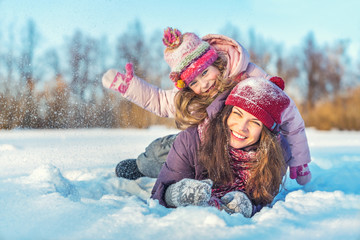 Little girl and her mother playing outdoors at sunny winter day. Active winter holydays concept.