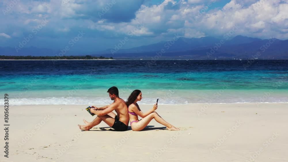 Young Happy Couple Sitting Back To Back While Reading Books in Ko Samui Island, Thailand - Wide Shot Young Happy Couple Sitting Back To Back While Reading Books in Ko Samui Island, Thailand - Wide Shot