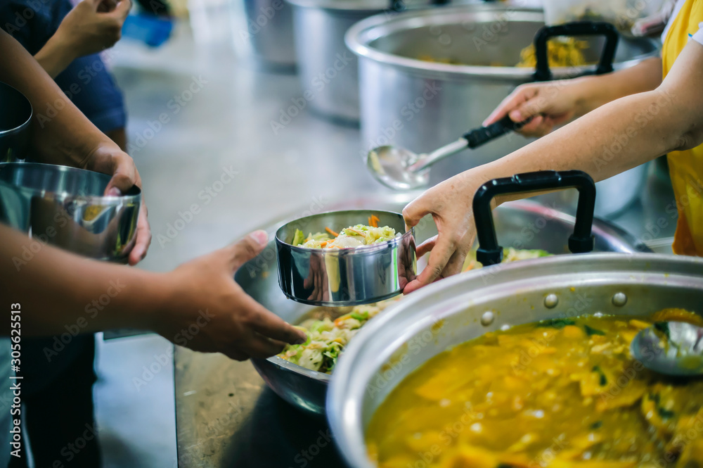 The hands of the needy holding a container to receive free charity food from volunteers : the concept of food assistance The hands of the needy holding a container to receive free charity food from volunteers : the concept of food assistance
