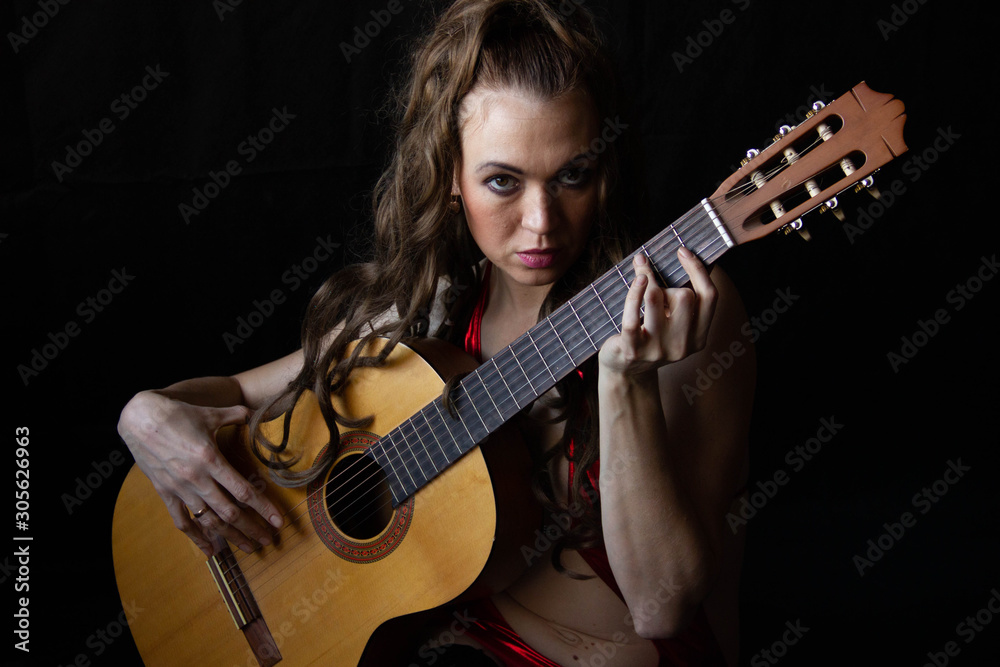 Obraz premium girl in a red dress sits on the floor near the guitar on a black background