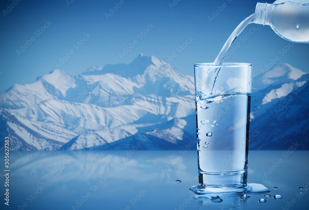 Pouring mineral water from bottle into a glass with water drops in the