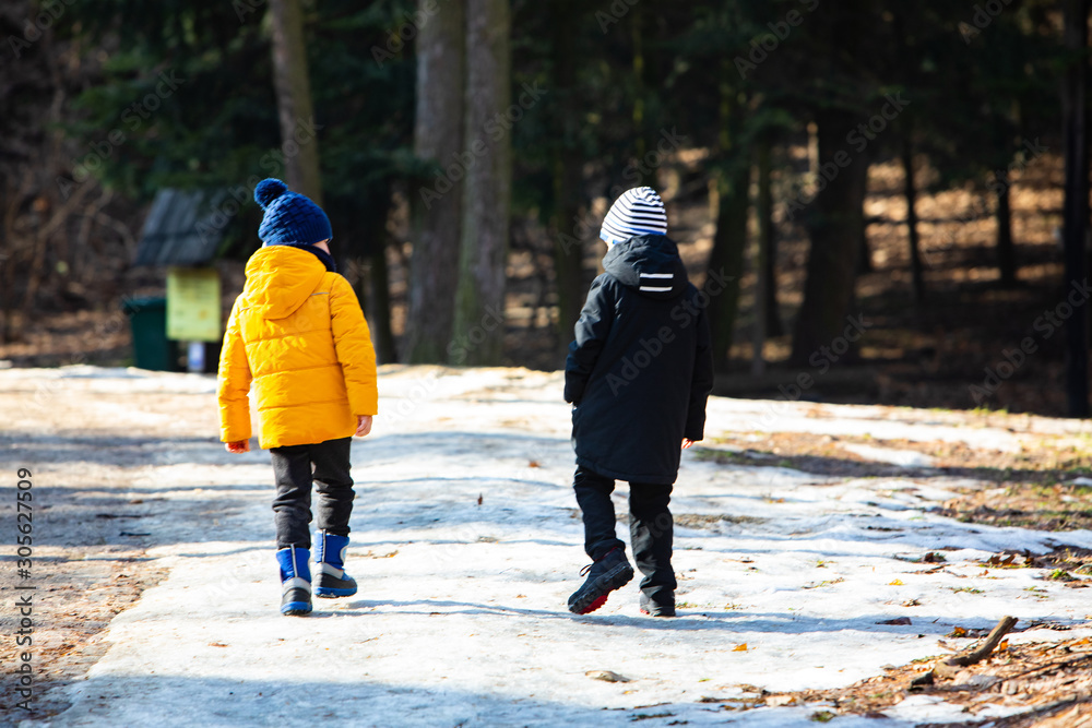 two boys in winter clothes walking by snowed park two boys in winter clothes walking by snowed park