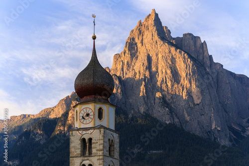 Sunrise landscapes of Church St. Valentin on grassy hilltop with view of rugged peaks of Mountain Schlern with alpenglow in background in the valley of South Tyrol, Italy, Europe photo