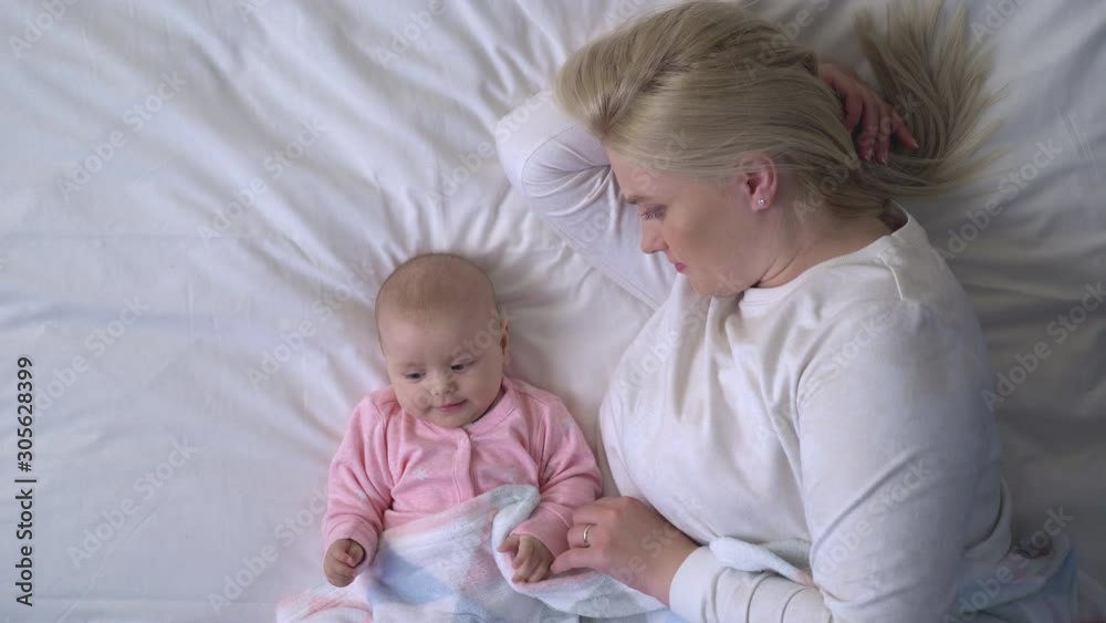 Happy mother lying with baby in bed active infant playing with blanket, nap time Happy mother lying with baby in bed active infant playing with blanket, nap time