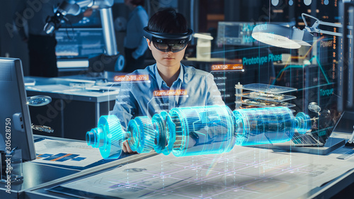 Industrial Factory Chief Engineer Wearing AR Headset Designs a Prototype of an Electric Motor on the Holographic Projection Blueprint. Futuristic Virtual Design of Mixed Technology Application. photo