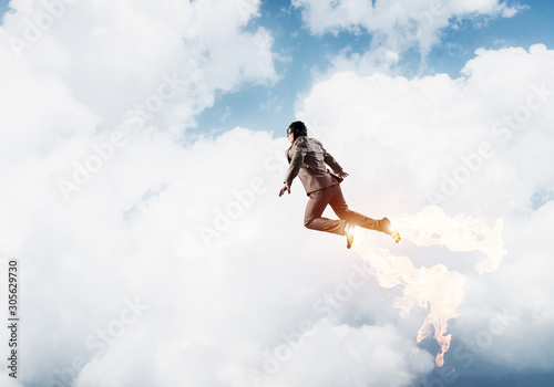 Businessman in suit and aviator hat flying in sky