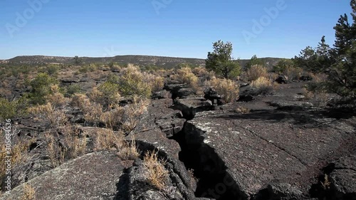Windy day at Lava Falls Trail in El Malpais, New Mexico. The large crevice was created by hardened lava in the ancient desert. Large cooled lava areas line the arid environment and brush blows in wind