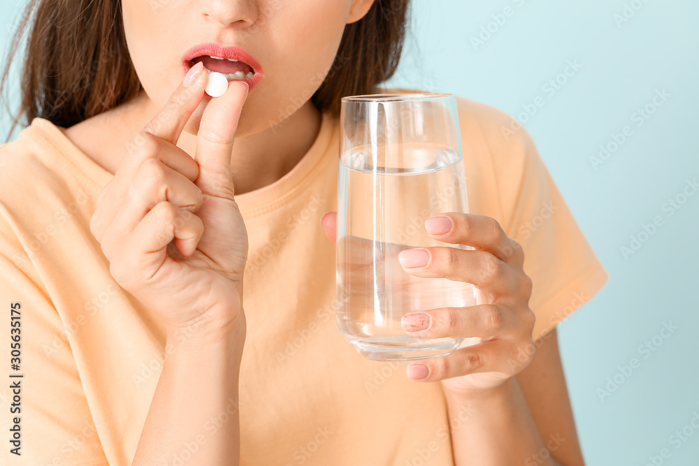 Young woman taking medicine on color background, closeup Young woman taking medicine on color background, closeup