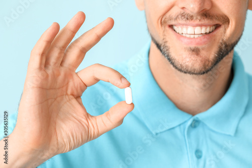 Man with pill on color background, closeup