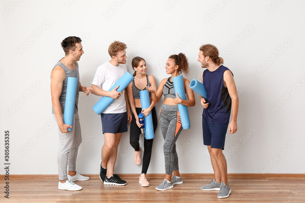 Fototapeta premium Group of people with yoga mats near light wall