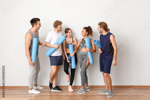 Group of people with yoga mats near light wall