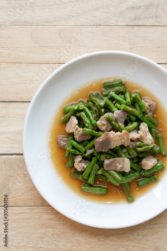 Fried yardlong beans with streaky pork in white dish on wooden table.