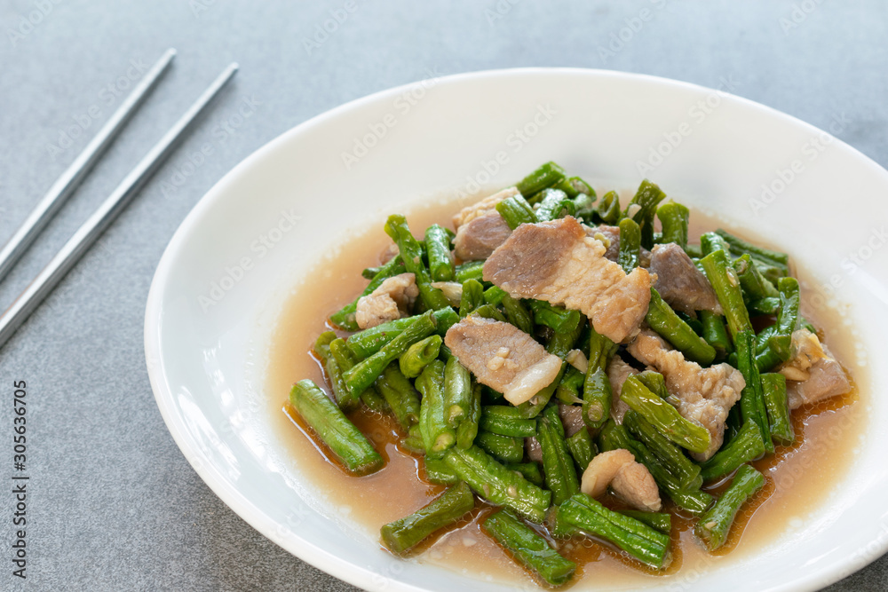 Fried yardlong beans with streaky pork in white dish on concrete table.