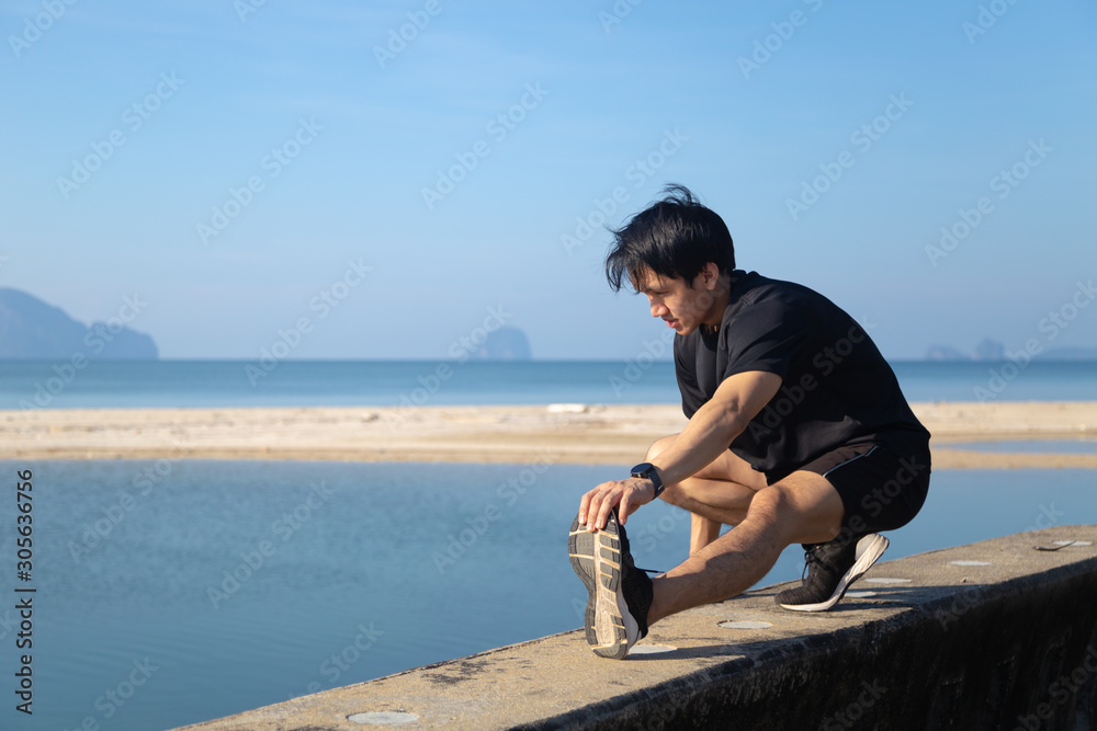 Asian male is stretching before doing work out ,jogging at seaside in the moring with beautiful sea view Asian male is stretching before doing work out ,jogging at seaside in the moring with beautiful sea view
