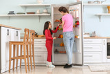 Little girl and her mother choosing food from fridge in kitchen