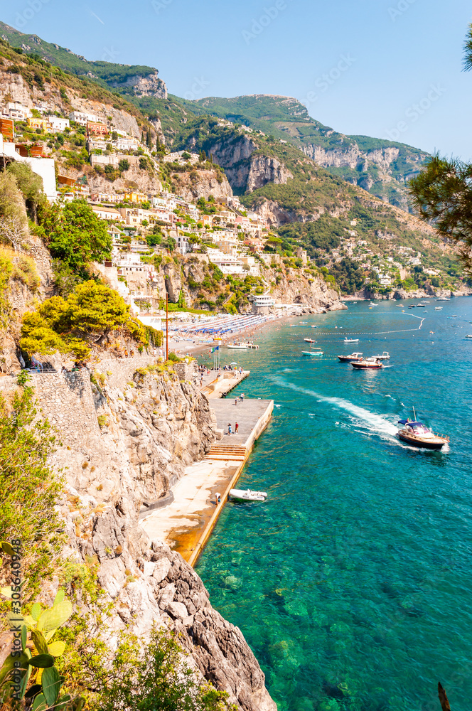 Amazing Italian Positano cityscape on rocky landscape, people on the beach, boats are coming and going to the sea tours, promenades full of apartments and businesses