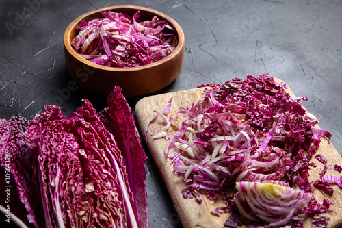 Chopped Red Chinese cabbage (Purple wombok) on wooden cutting board and bowl on stone table. Red Napa cabbage with vibrant colored leaves on black background. Cooking vegetable salad, healthy food