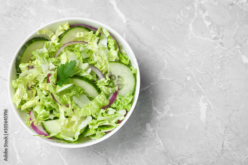Tasty salad with cabbage and cucumbers on light grey marble table  top view. Space for text