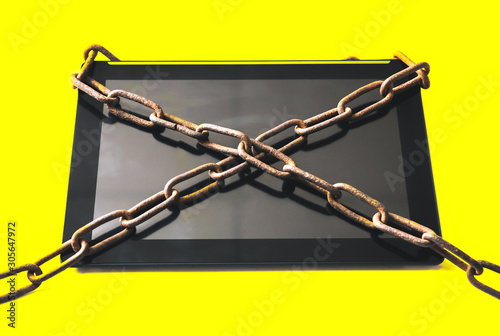 Rusty chains around the tablet. Isolated on yellow background. Addicted to modern technologies.