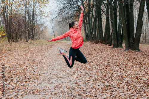 Young happy woman jumping in autumn park. Fitness girl training outside on a warm fall day
