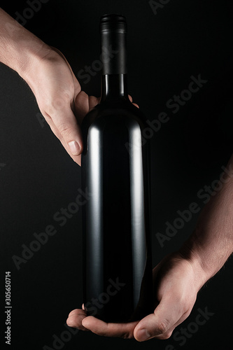 Red wine bottle in the hands of men. Isolated on black exquisite background.