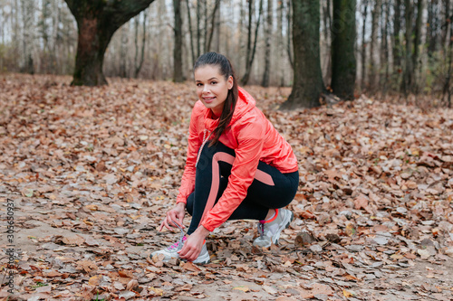 runner woman tying laces for autumn run in forest park