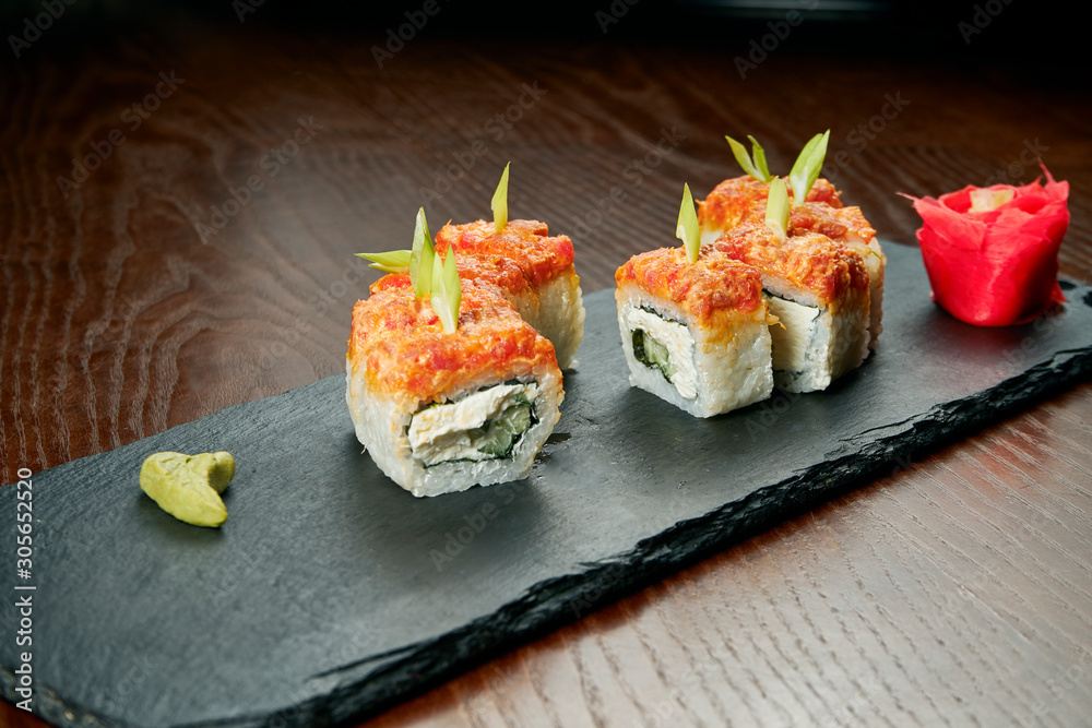 Sushi rolls with cucumber, philadelphia cheese, caviar and salmon on a black slate board on a wooden background. Japanese cuisine. Close up Sushi rolls with cucumber, philadelphia cheese, caviar and salmon on a black slate board on a wooden background. Japanese cuisine. Close up