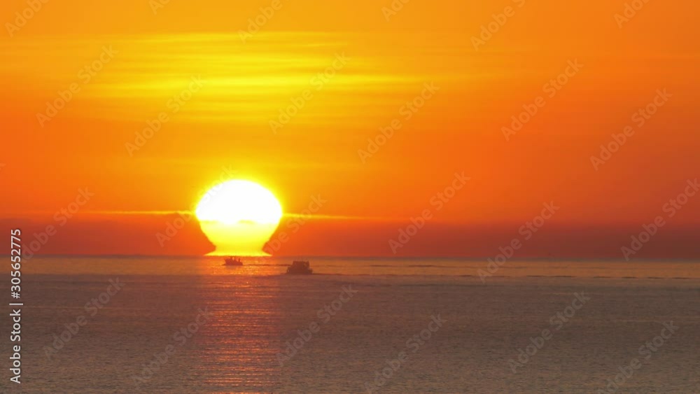 Breathtaking orange sunrise over  ocean horizon with boats silhouetted against glowing sea