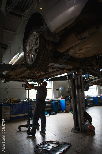 Car repair in the service station. Hands of a mechanic in overalls repairing the car on the lift without wheel, holding the tire and mechanical works.