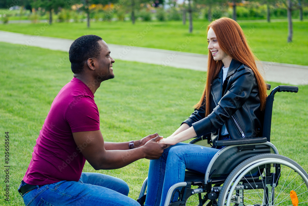 afro american man marriage proposal giving a ring to his redhaired ginger girlfriend.she sitting on wheel chair and surprised and amazed afro american man marriage proposal giving a ring to his redhaired ginger girlfriend.she sitting on wheel chair and surprised and amazed