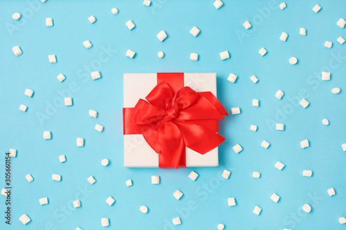 Christmas gift box with red ribbon and marshmallows on light background
