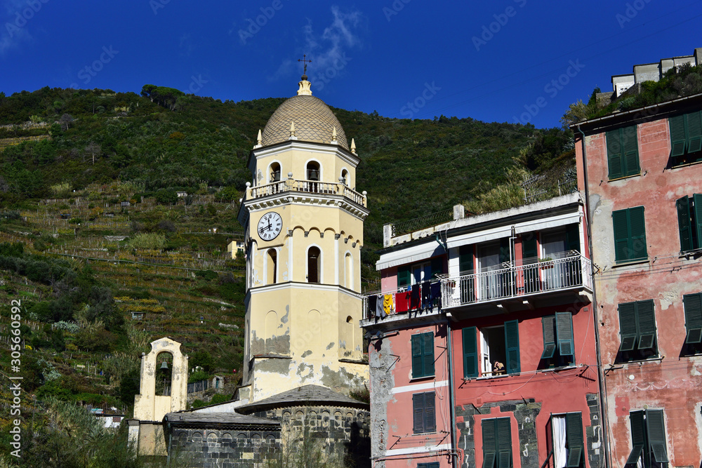 Medieval church surrounded by colorful italian buildings and green agriculture terrasses of the Vernazza village of Cinque Terre under daylight. Italy 2019.
