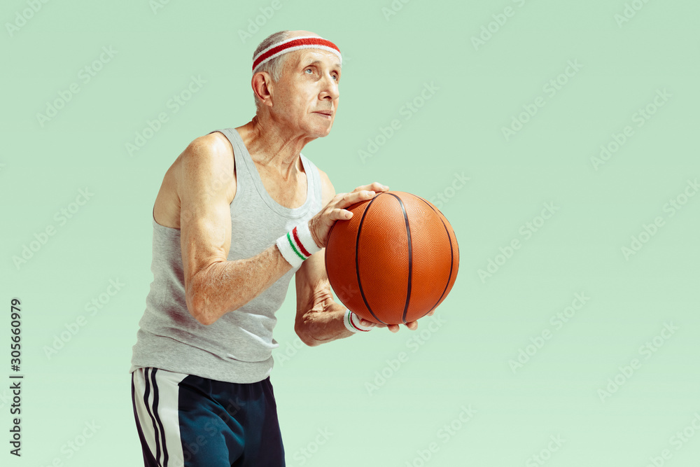 Naklejka premium Senior man wearing sportwear playing basketball isolated on green background. Caucasian man in great shape stays active and sportive. Concept of sport, activity, movement, wellbeing. Copyspace, ad.