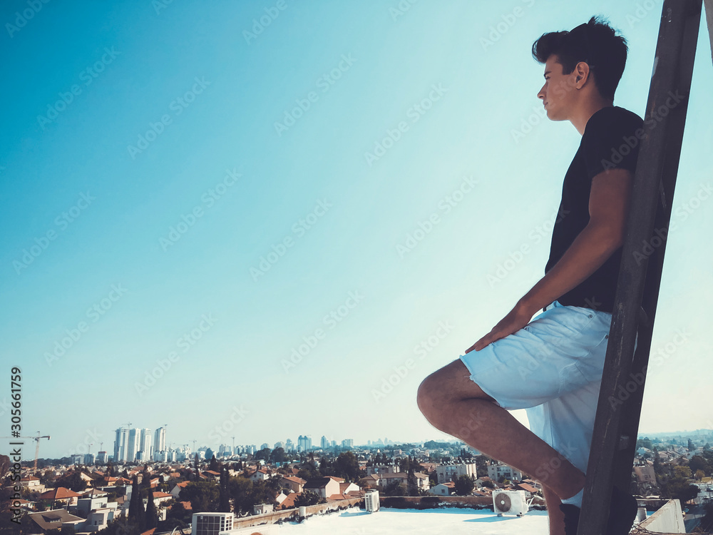 Young attractive man posing in front of camera on the roof of a residential building standing on a ladder