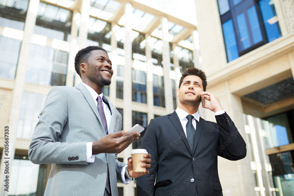 Two successful business managers in suits using mobile phones and busy the conversation while walking in the city Two successful business managers in suits using mobile phones and busy the conversation while walking in the city