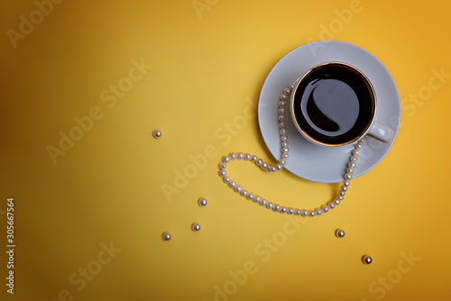 A cup of espresso, pearl beads and a few beads are on a yellow background. Flatlay