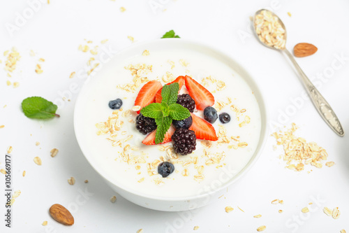 Greek yogurt with granola fresh strawberries, blueberries, blackberries and almonds on white table. Healthy snack. Breakfast food. 