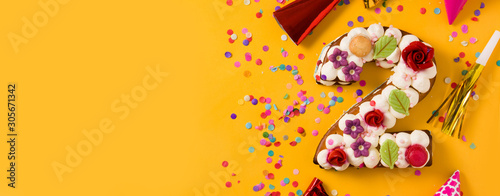 Number two cake decorated with flowers, macarons and confetti isolated on yellow background. Panorama view