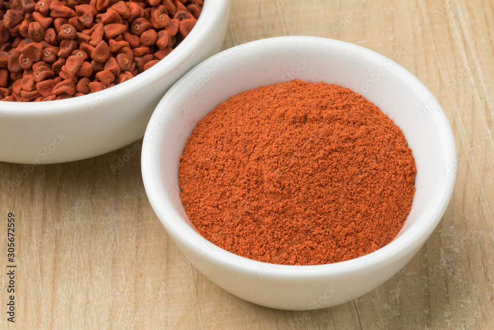 Bowl with dried Annatto seeds and a bowl with ground Annatto powder Bowl with dried Annatto seeds and a bowl with ground Annatto powder