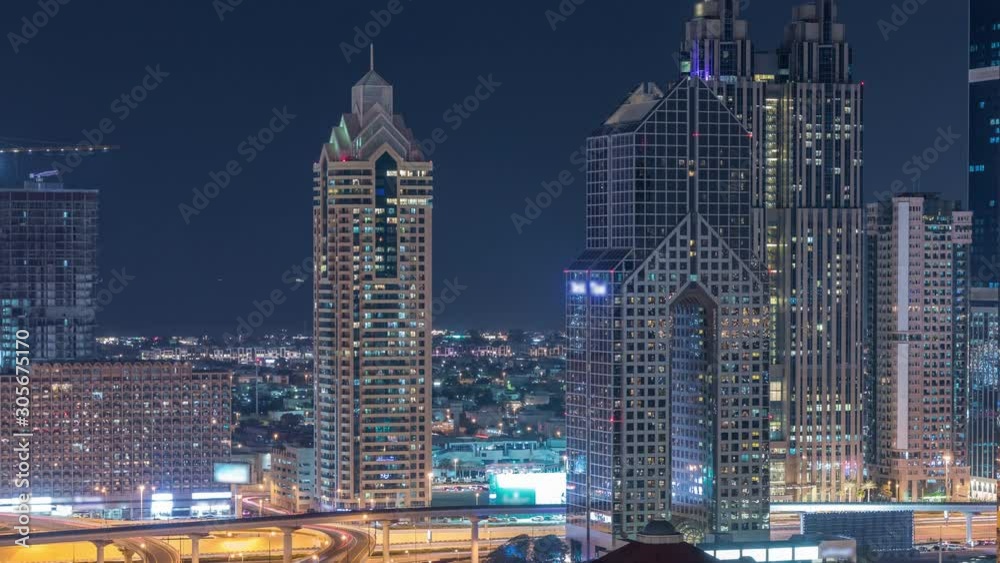 Aerial view of illuminated skyscrapers and road junction in Dubai night timelapse. Traffic on intersection in downtown with modern towers around. Cloudy sky Aerial view of illuminated skyscrapers and road junction in Dubai night timelapse. Traffic on intersection in downtown with modern towers around. Cloudy sky