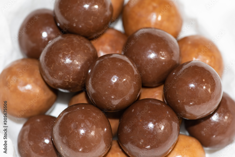Dark and milk chocolate covered balls. Malted milk balls on plate with white paper. Round candy caramel. Selective focus. Dark and milk chocolate covered balls. Malted milk balls on plate with white paper. Round candy caramel. Selective focus.