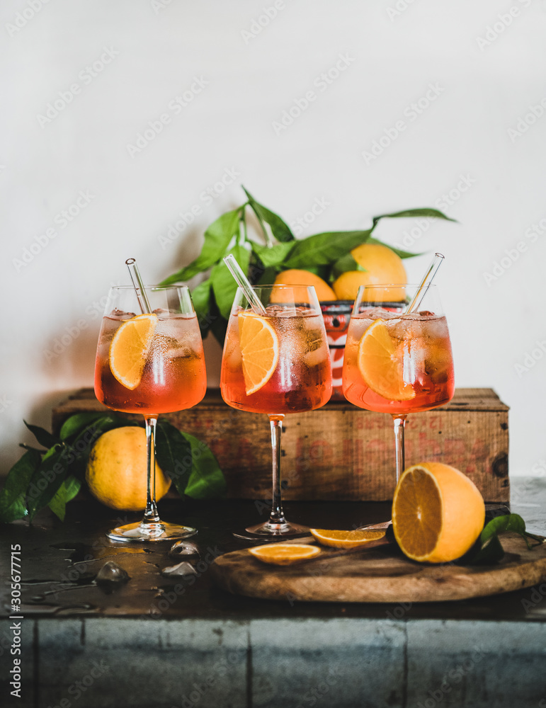Foto Stock Aperol Spritz aperitif alcohol cold drink with oranges and ice  cubes in glasses with eco-friendly glass straws on concrete table, white  wall at background, copy space. Summer refreshing drink concept