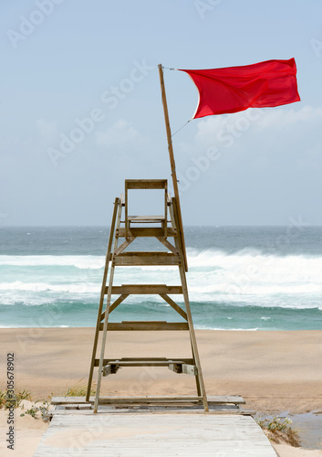 Silla de socorrista vacía con bandera roja ondeando al viento