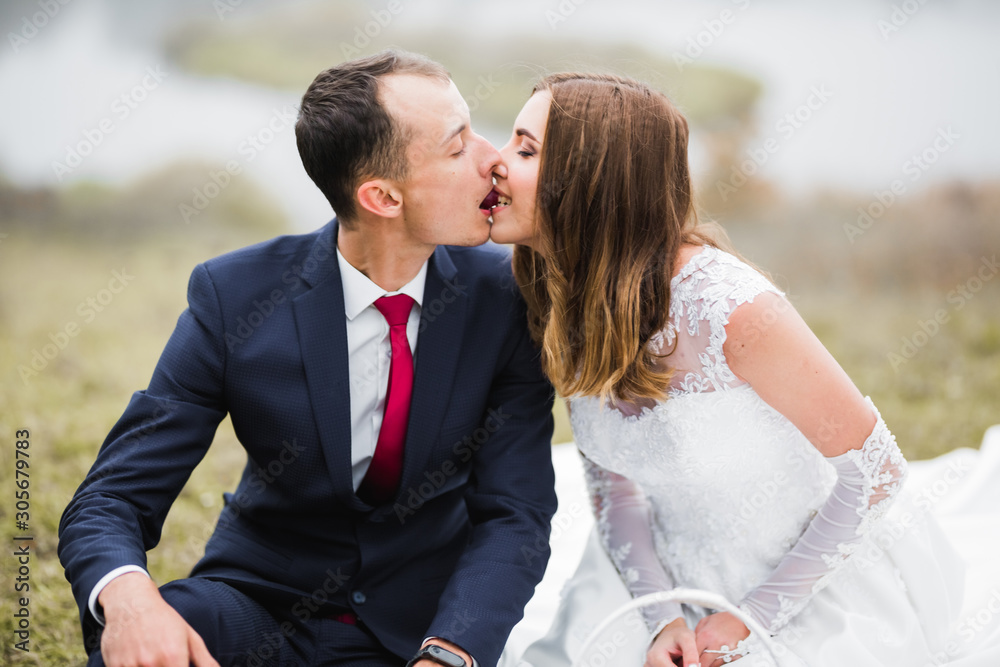Beautiful bride and groom embracing and kissing on their wedding day outdoors Beautiful bride and groom embracing and kissing on their wedding day outdoors