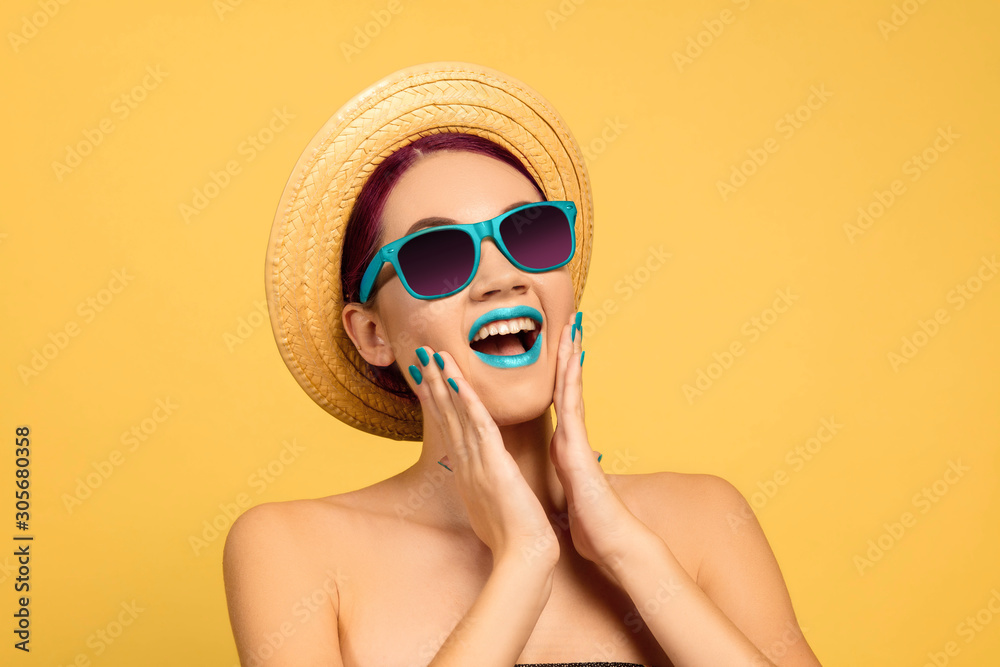 Φωτογραφία Portrait of beautiful woman with bright make-up, hat and sunglasses on yellow studio background