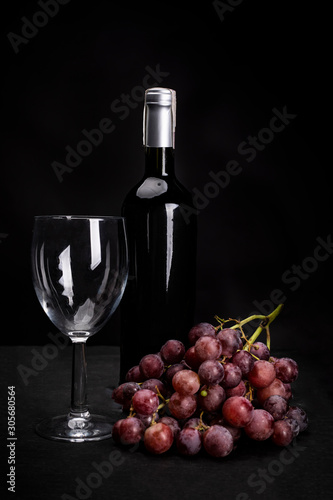 An elegant composition of bottle of wine, bunch of grapes and a glass on a dark background. A studio photo.